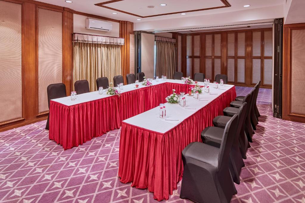 a conference room with long tables with red curtains and chairs at The Ummed Ahmedabad Airport in Ahmedabad