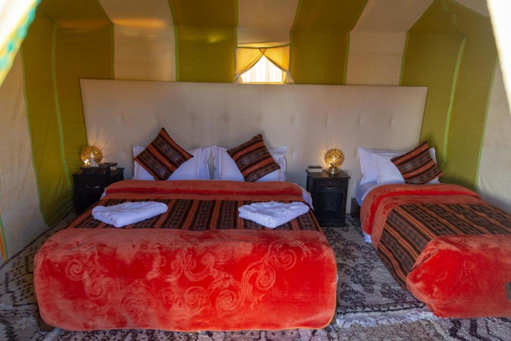 a bedroom with two beds with red covers at Sahara Desert Luxury Camp in Merzouga