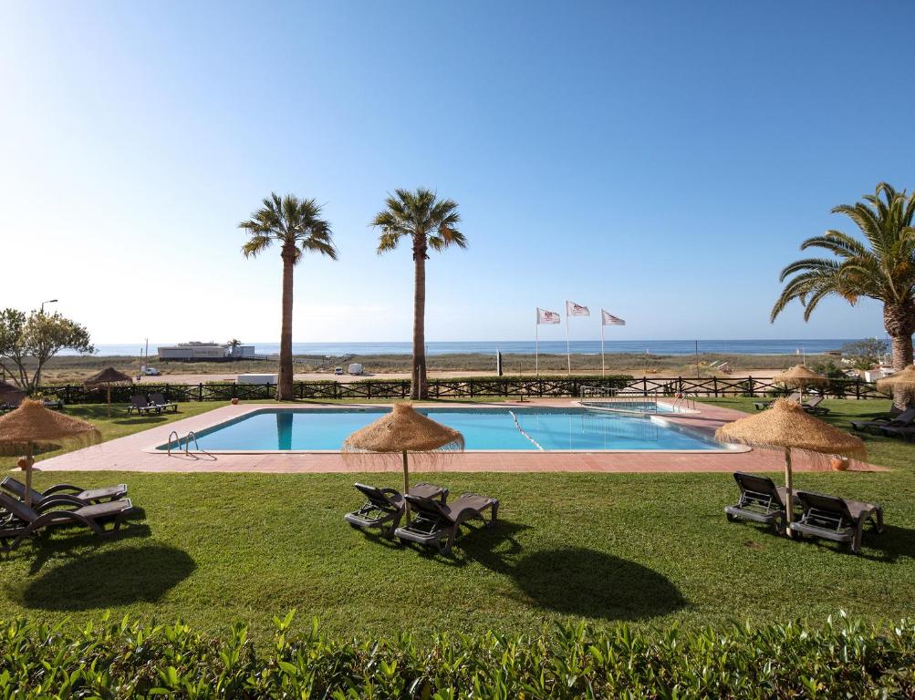 a pool with chairs and palm trees and the ocean at Dom Pedro Lagos in Lagos