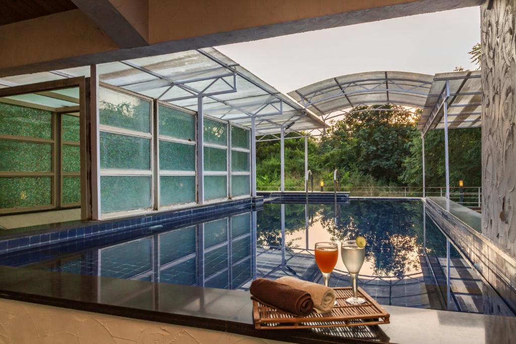 einen Pool mit einem Glashaus mit einem Tisch und Weingläsern in der Unterkunft SaffronStays Bellini, Karjat in Kalamb