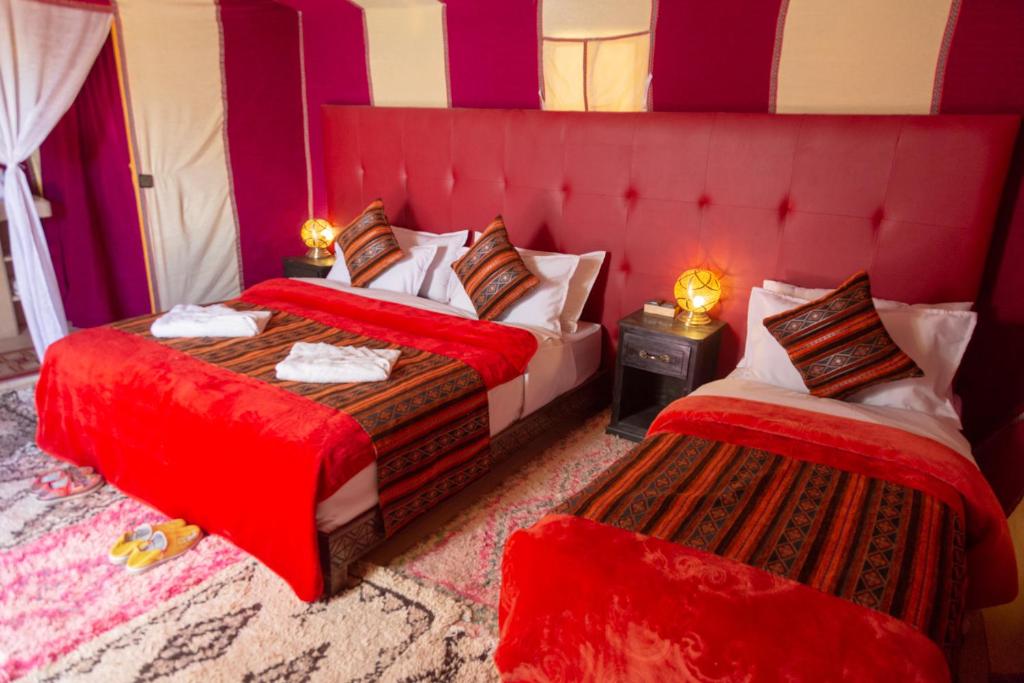 a bedroom with two beds with red sheets at Sahara Desert Luxury Camp in Merzouga