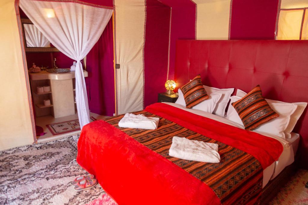 a bedroom with a red bed with towels on it at Sahara Desert Luxury Camp in Merzouga