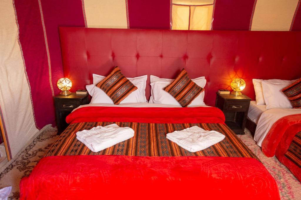 a red room with two beds with towels on them at Sahara Desert Luxury Camp in Merzouga