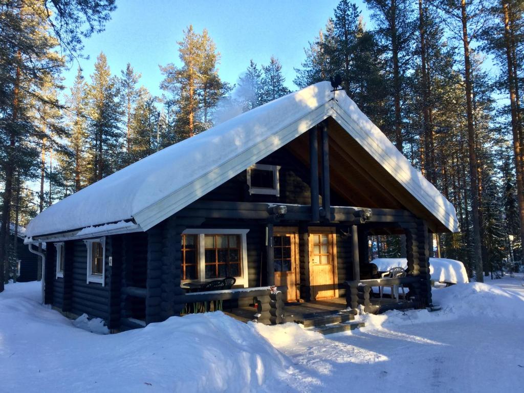 uma cabana de madeira com um telhado coberto de neve na neve em Villa Luppopirtti em Luosto