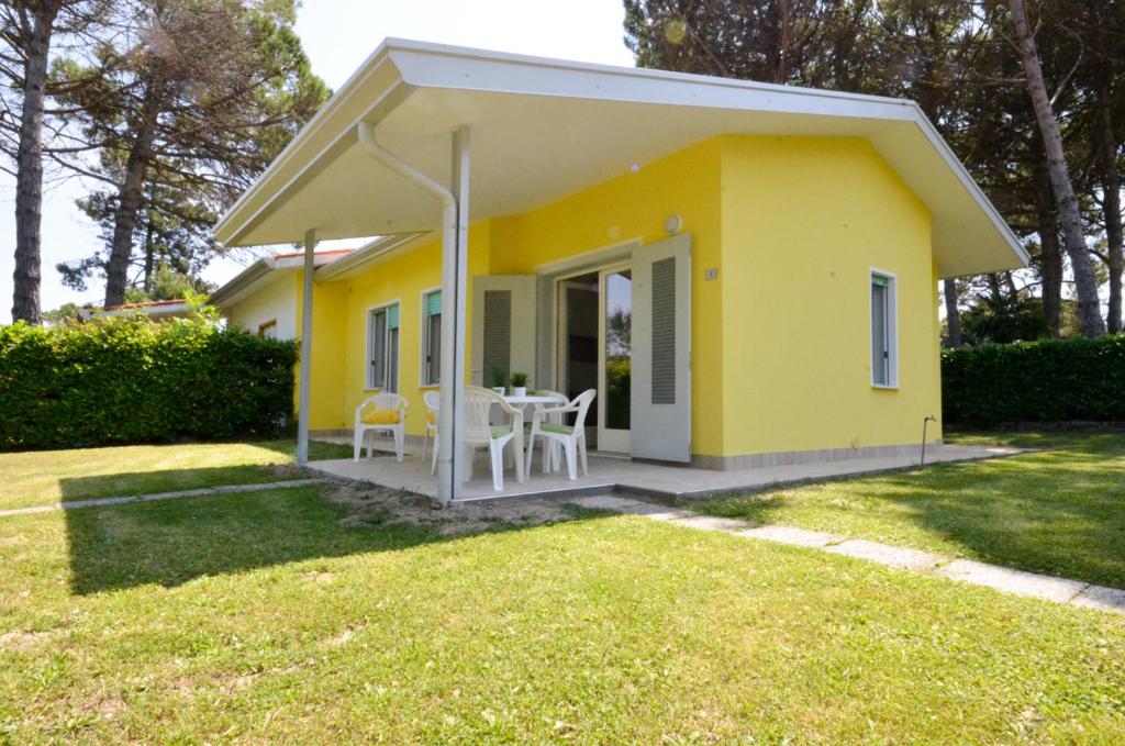 a yellow house with a table and chairs in a yard at Ville Dogi Sud in Bibione