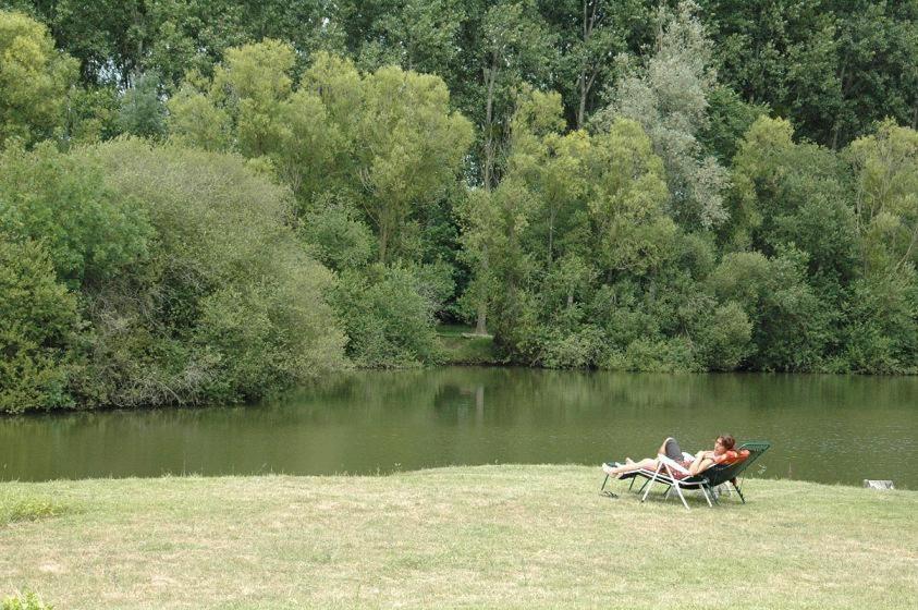 dos personas sentadas en una silla cerca de un lago en L&#39;Autourserie, en Chahaignes