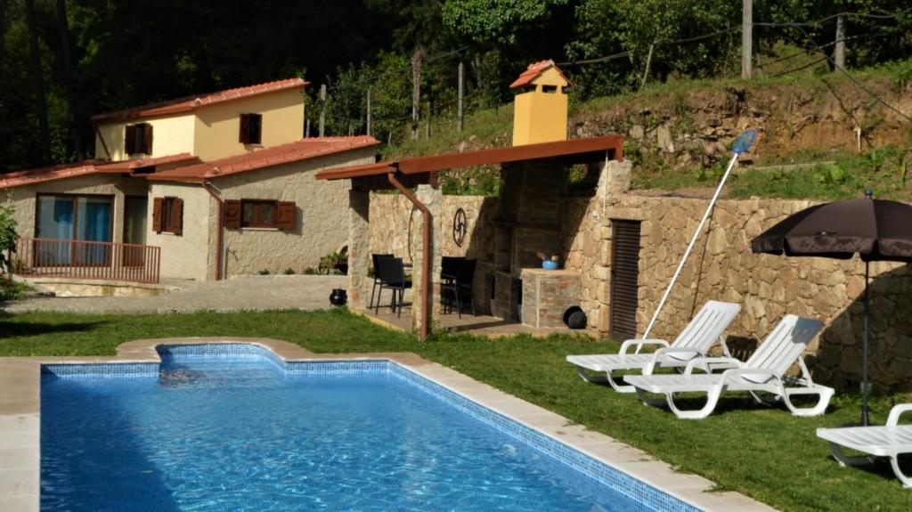 ein Pool mit Stühlen und einem Sonnenschirm und ein Haus in der Unterkunft Casa do Ribeiro in Sever do Vouga