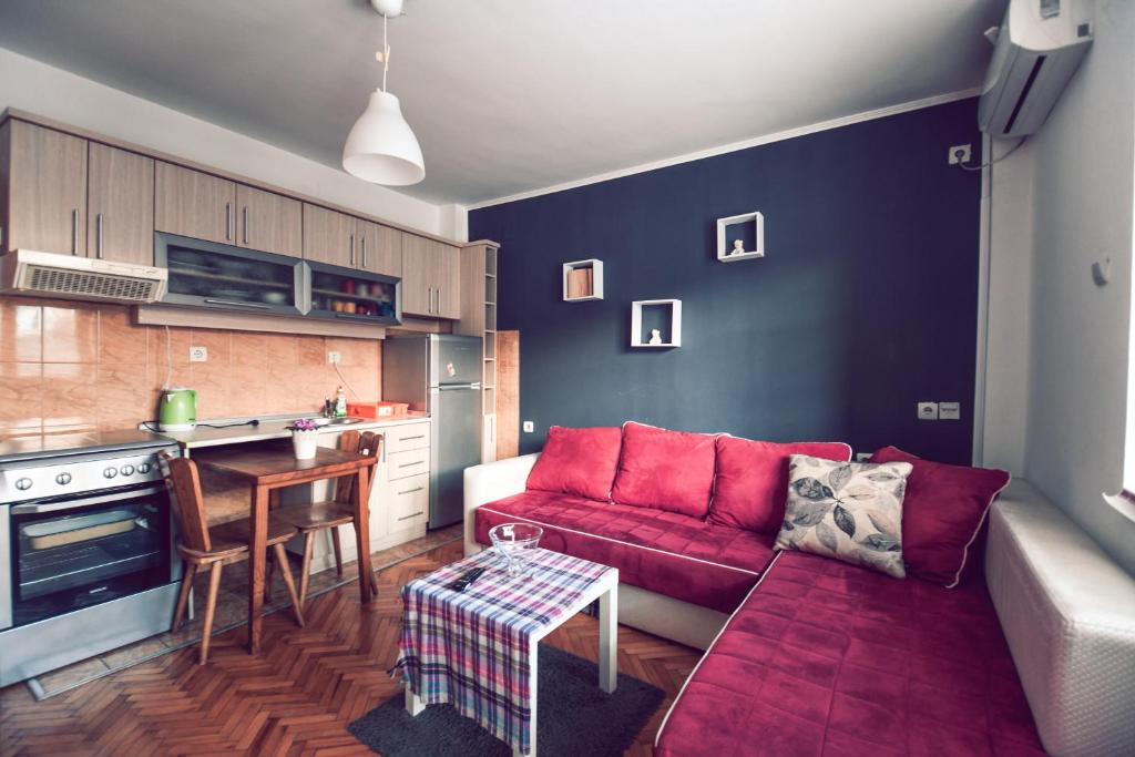 Square Vanilla Apartments في إسكوبية: غرفة معيشة مع أريكة حمراء ومطبخ
