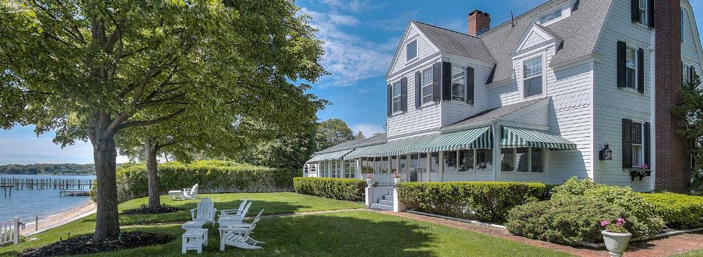 a large white house with tables and chairs next to the water at Harbor Knoll Bed and Breakfast in Greenport
