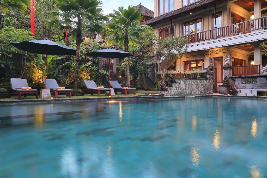 a swimming pool with chairs and umbrellas in front of a building at Ketut's Place Villas Ubud in Ubud