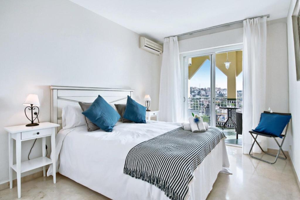 a white bedroom with a bed with blue pillows and a window at Del Parque Flats - Torrevigia in Cala del Moral