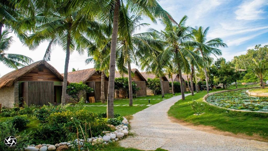 a path to a resort with palm trees and a pond at Casa Marina Resort in Quy Nhon