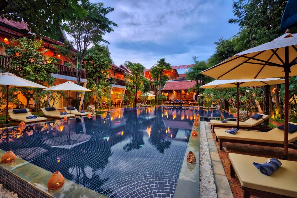 uma piscina num hotel com mesas e guarda-sóis em Mane Village Suites em Siem Reap