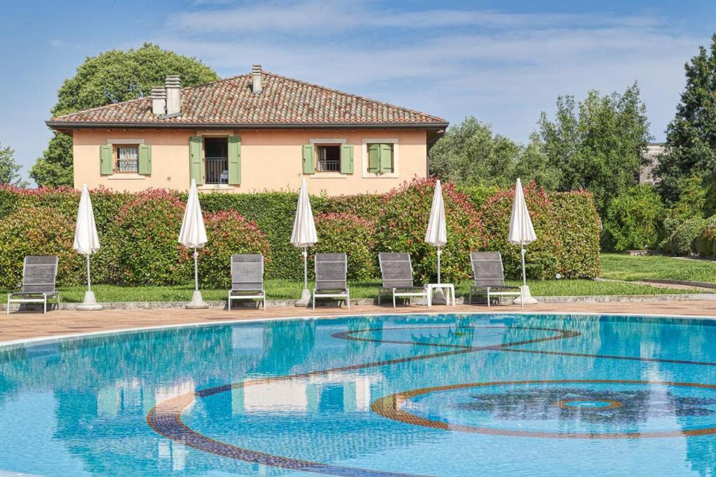 ein Pool mit Sonnenschirmen und Stühlen sowie ein Haus in der Unterkunft Active Hotel Paradiso & Golf in Peschiera del Garda