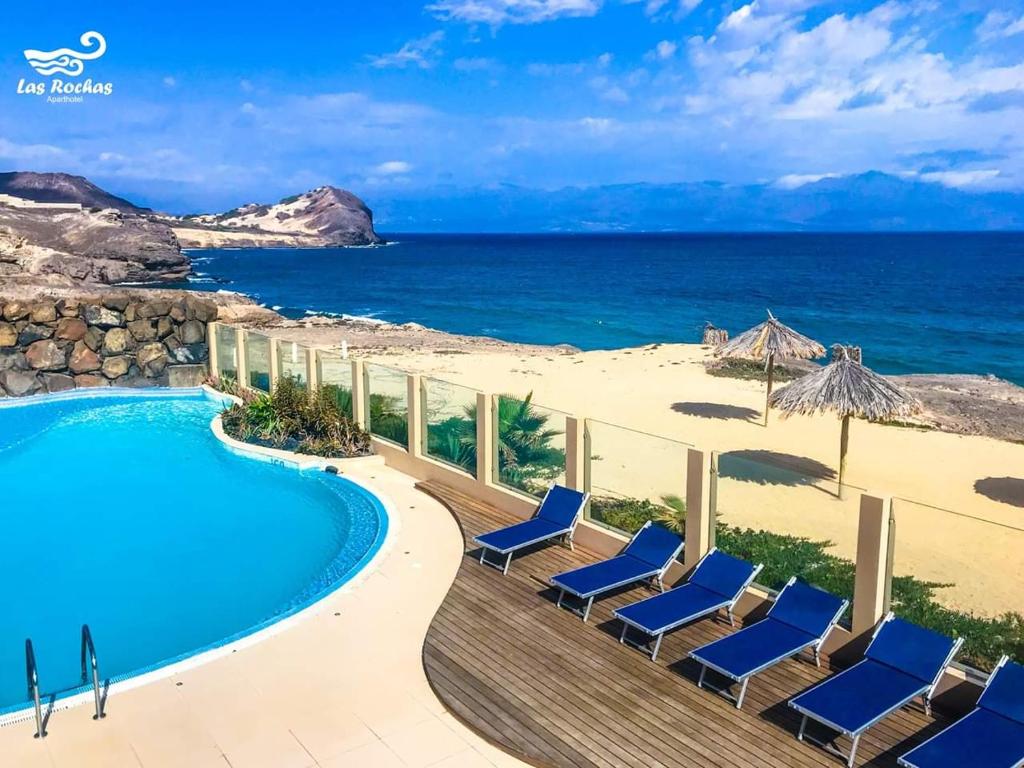a resort with a swimming pool and chairs and the ocean at Las Rochas in Mindelo