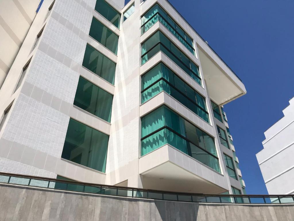 a tall white building with green windows at Sophia II Residence Inn in Arraial do Cabo