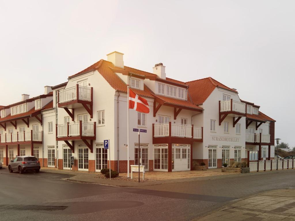 un grand bâtiment blanc avec un drapeau devant lui dans l'établissement Strandhotellet, à Blokhus