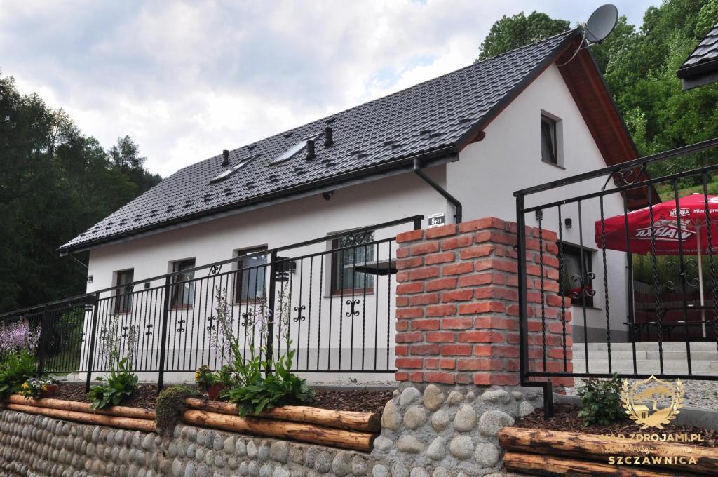 una pequeña casa blanca con una valla negra en "Nad Zdrojami" Domek Kowalczyk 691-739-603, en Szczawnica