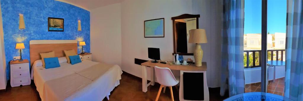 a bedroom with a bed and a desk and a window at Hotel las Calas in Agua Amarga