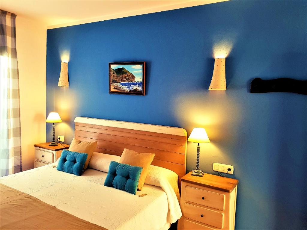 a bedroom with a bed with blue walls and two lamps at Hotel las Calas in Agua Amarga