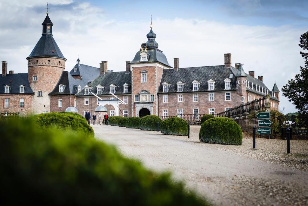 a large red brick building with a tower at Romantik Parkhotel Wasserburg Anholt in Isselburg