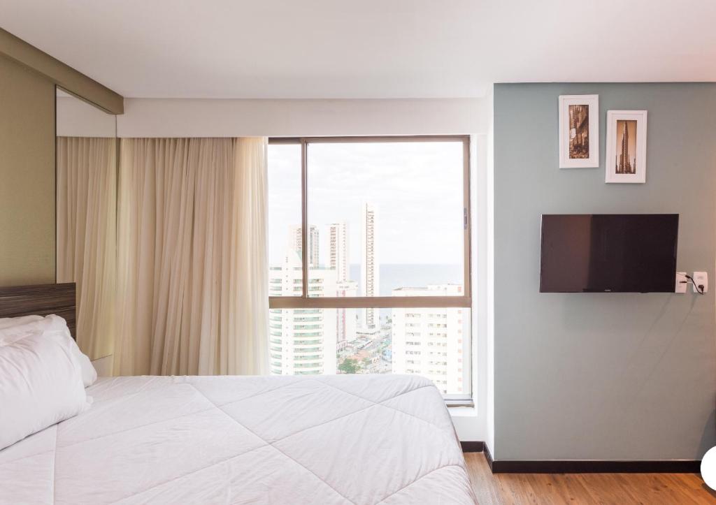 1 dormitorio con cama blanca y ventana grande en LOFT PREMIUM Boa Viagem 20 andar, en Recife