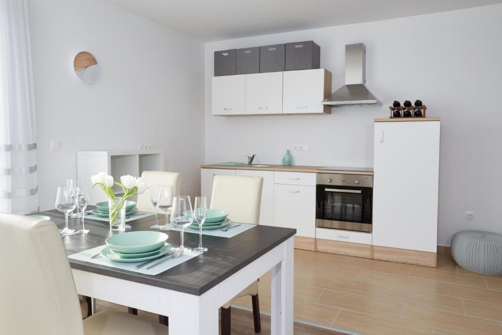 a white kitchen with a table with plates and wine glasses at Panorama Apartmanok in Villány