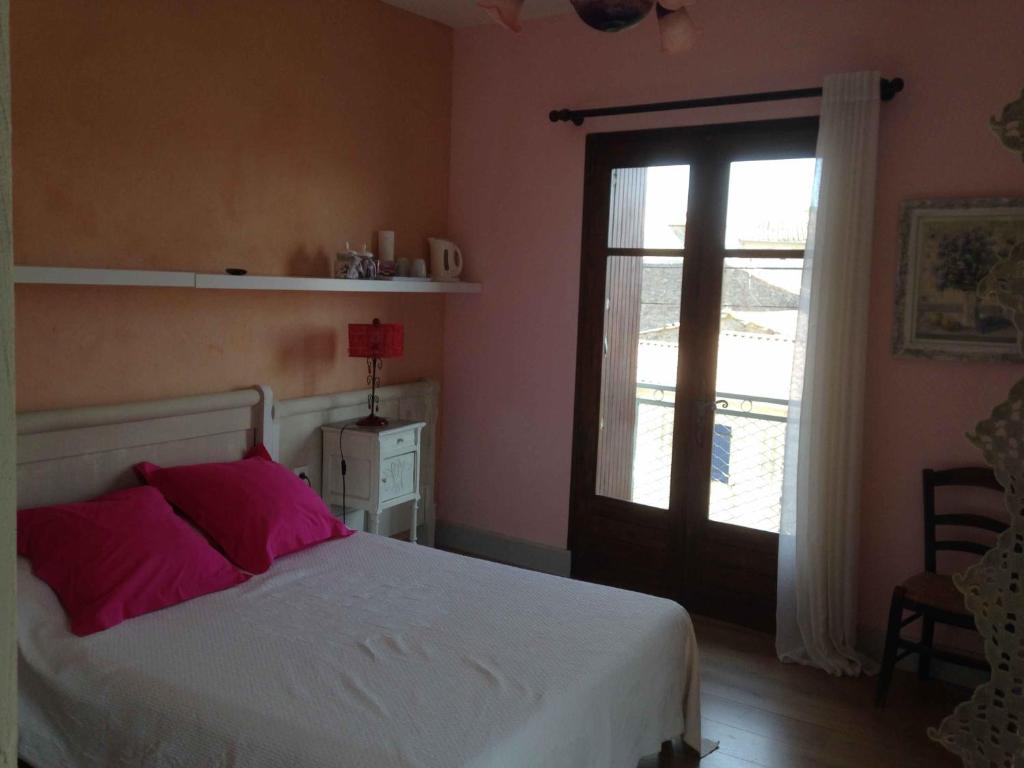 sypialnia z łóżkiem z różowymi poduszkami i oknem w obiekcie Chambre du Charron w mieście Azillanet