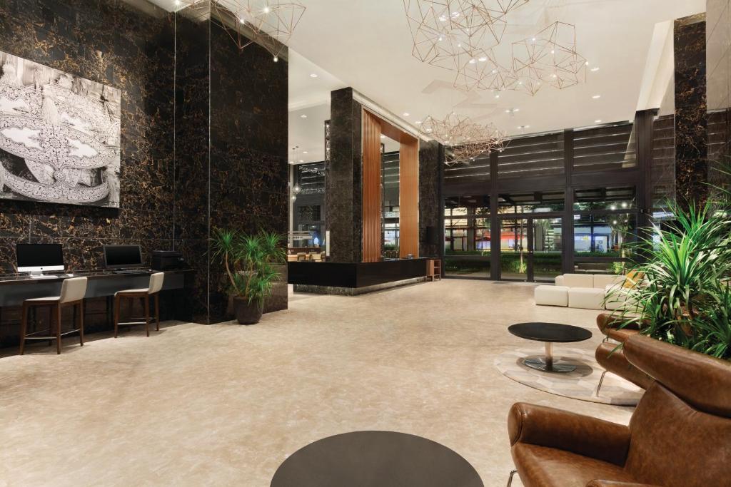 A grand hotel lobby with marble-look walls, reception workstations, plants, and lounge chairs.