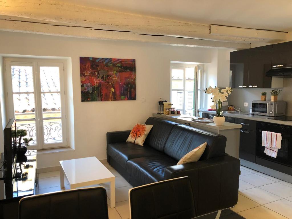 a living room with a black leather couch and a kitchen at À deux pas du Palais des Festivals , deux pièces dans le bas du quartier historique du Suquet à Cannes in Cannes