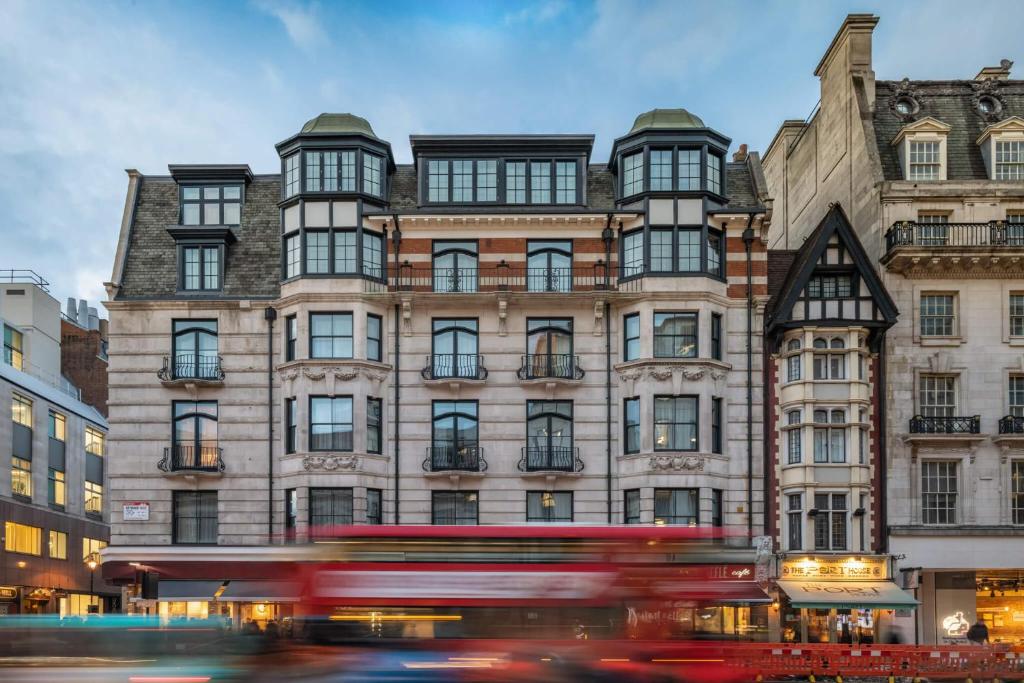 Ein roter Bus fährt an einem hohen Gebäude vorbei. in der Unterkunft The Resident Covent Garden in London