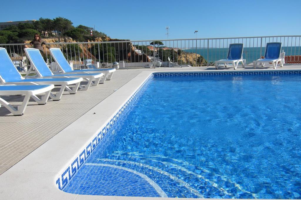 uma piscina com cadeiras azuis e o oceano em Duplex - Varandas Do Mar Patricia em Albufeira