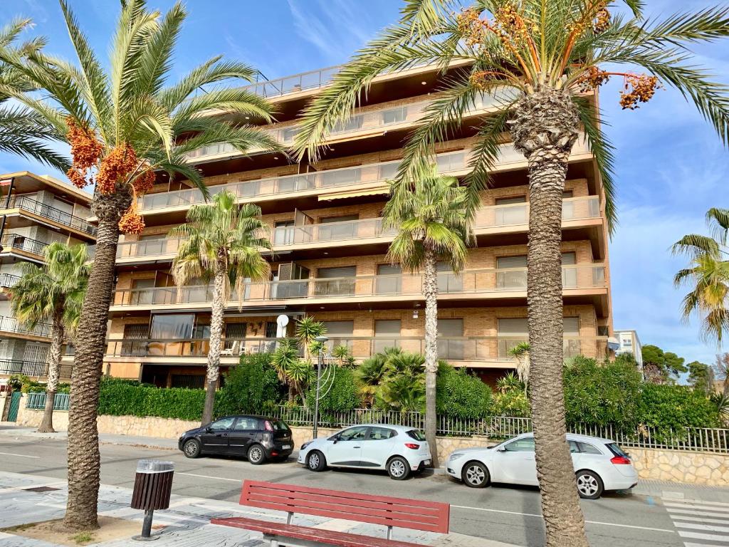 un banc rouge devant un bâtiment planté de palmiers dans l'établissement APARTAMENTO - WIFI FREE - FRENTE AL MAR, à Salou