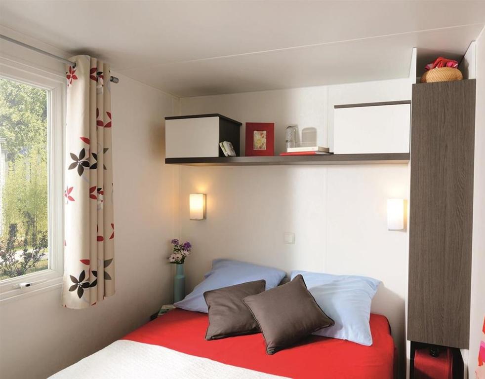 a bedroom with a bed with a red blanket and a window at Camping la Croix du Sud in Saint-Tropez