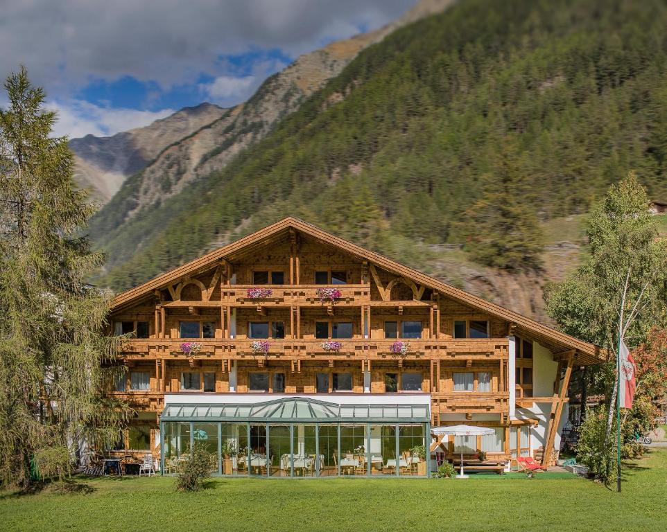 a large wooden building with mountains in the background at Hotel am Hof in Sölden