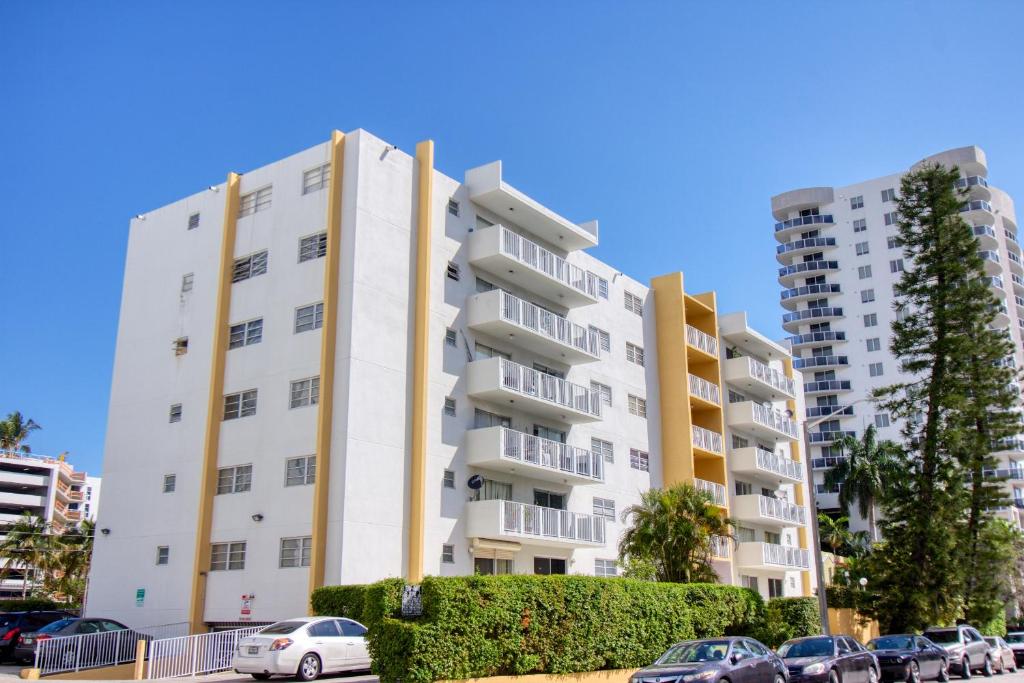 un immeuble d'appartements blanc avec des voitures garées dans un parking dans l'établissement 23 Palms Suites - Midtown Wynwood, à Miami