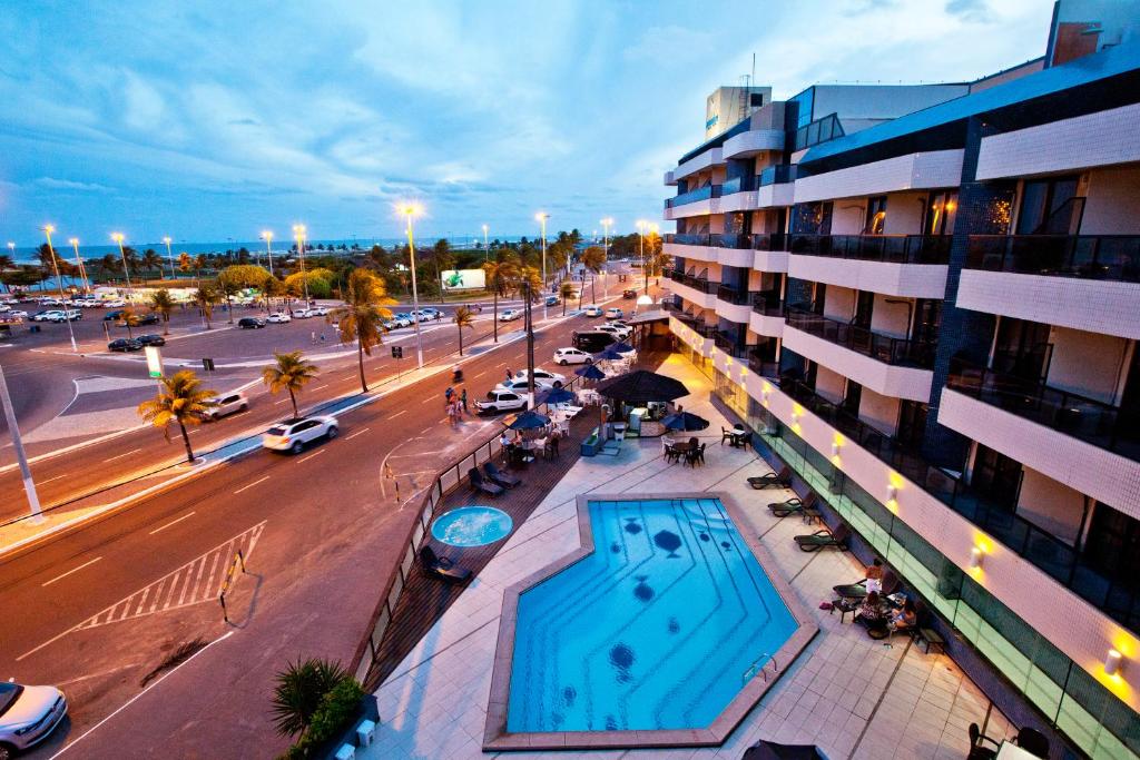 a building with a swimming pool next to a street at Aquarios Praia Hotel in Aracaju