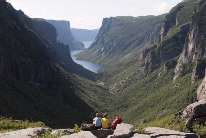 three people sitting on a rock overlooking a valley at The Rooms at Woody Point in Bonne Bay