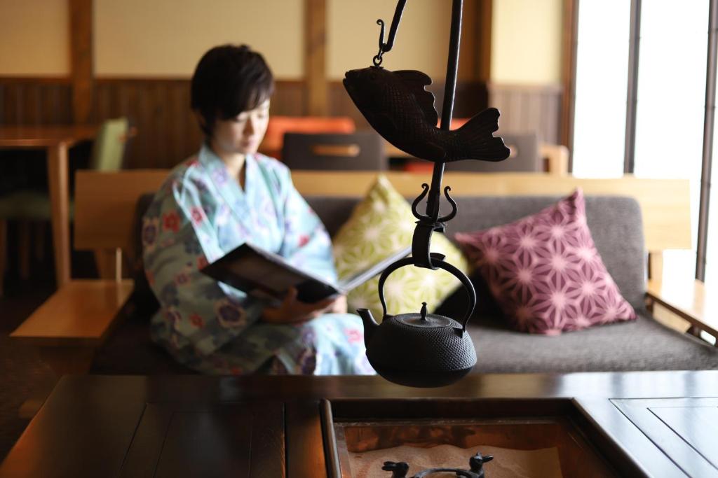 a person sitting on a couch reading a book at K's House Takayama Oasis [2nd K's Hostel] in Takayama