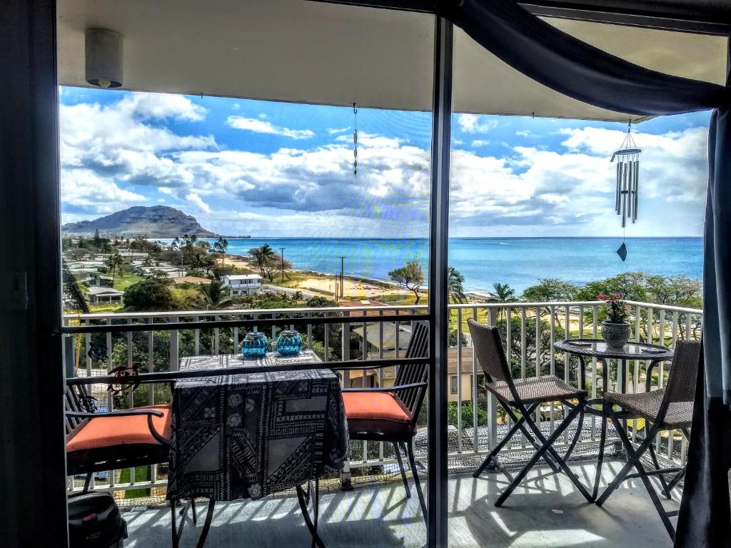 balcón con mesa, sillas y vistas al océano en Pokai Bay Penthouse Studio, en Waianae