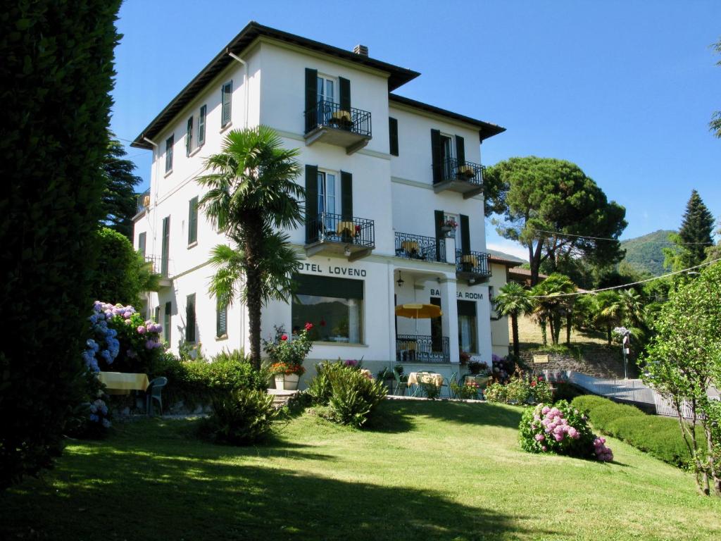 un grand bâtiment blanc avec un palmier en face dans l'établissement Hotel Loveno, à Menaggio