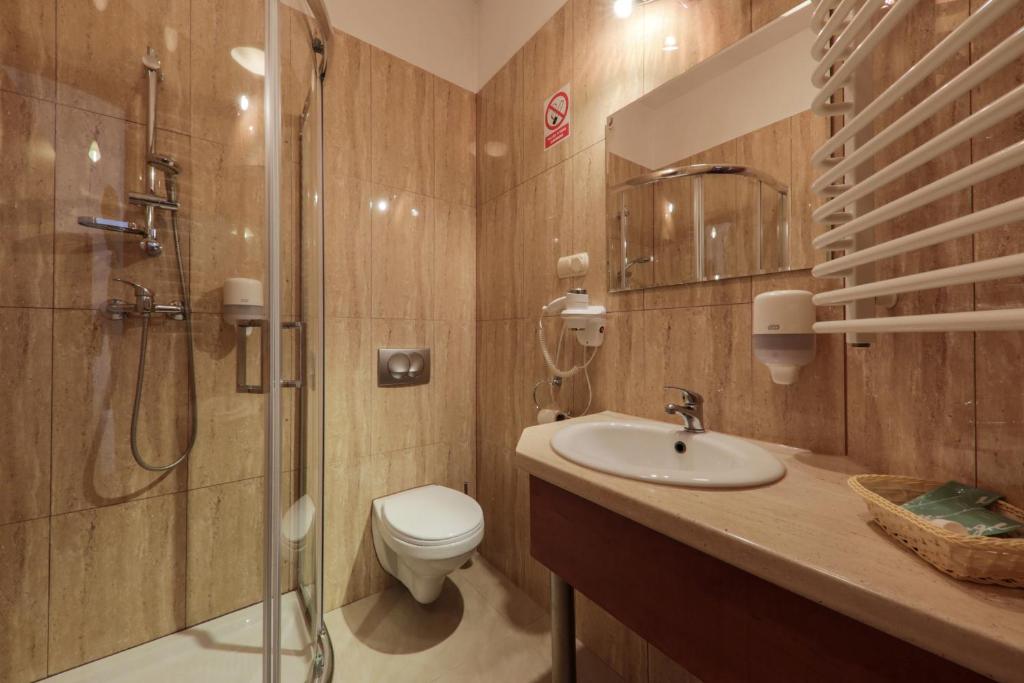 Compact tiled bathroom with corner shower, wall-mounted toilet, sink and white heated towel rack.