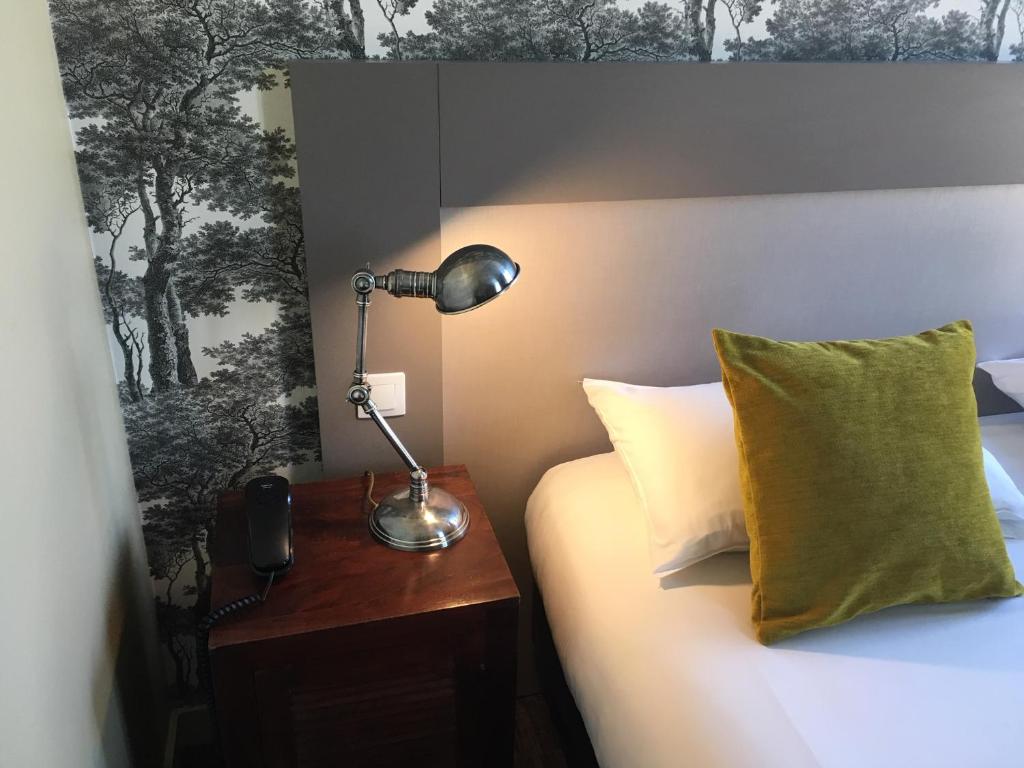 una lámpara en una mesita de noche junto a una cama en Logis Hôtel Le Vert Galant en La Flèche