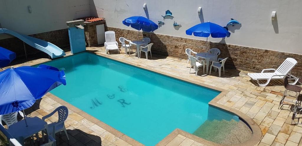 a swimming pool with blue umbrellas and chairs and a slide at Suítes Xodo Tour in Arraial do Cabo