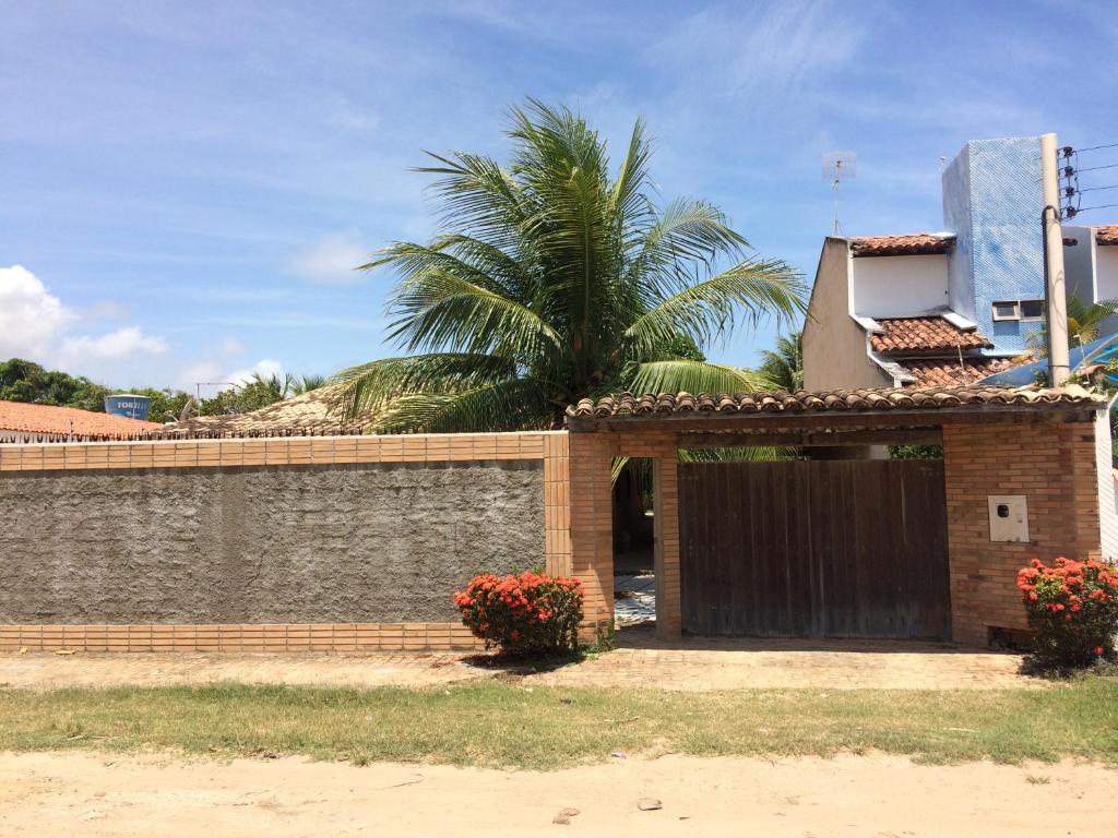 a brick house with a gate and a palm tree at Casa de Veraneio, com piscina, churrasqueira, área de lazer, três suites com ar condicionado a 100m da praia, na Barra de São Miguel-AL in Barra de São Miguel
