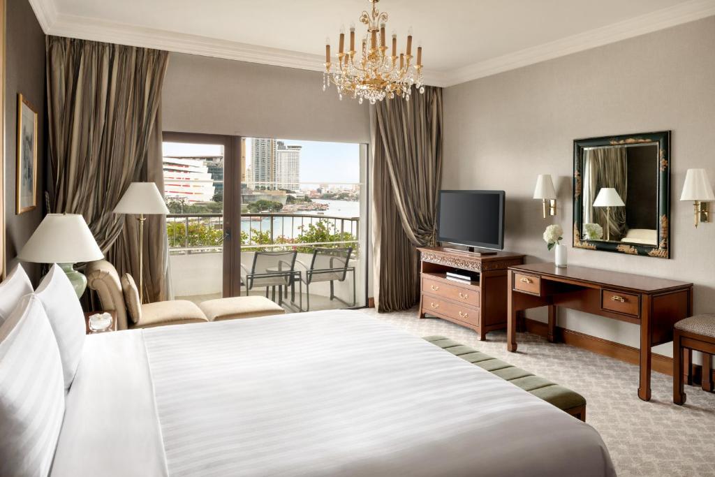 A traditional-style bedroom with a balcony, river view, chandelier, desk, and television.
