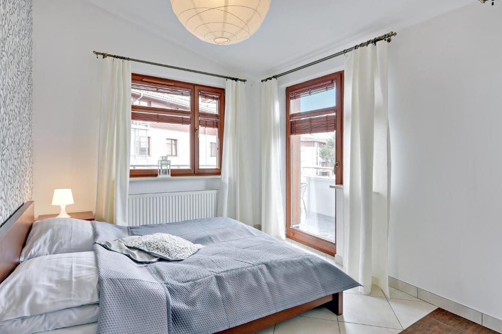 a bedroom with a bed and two windows at Grand Apartments - Neptun Park. in Gdańsk
