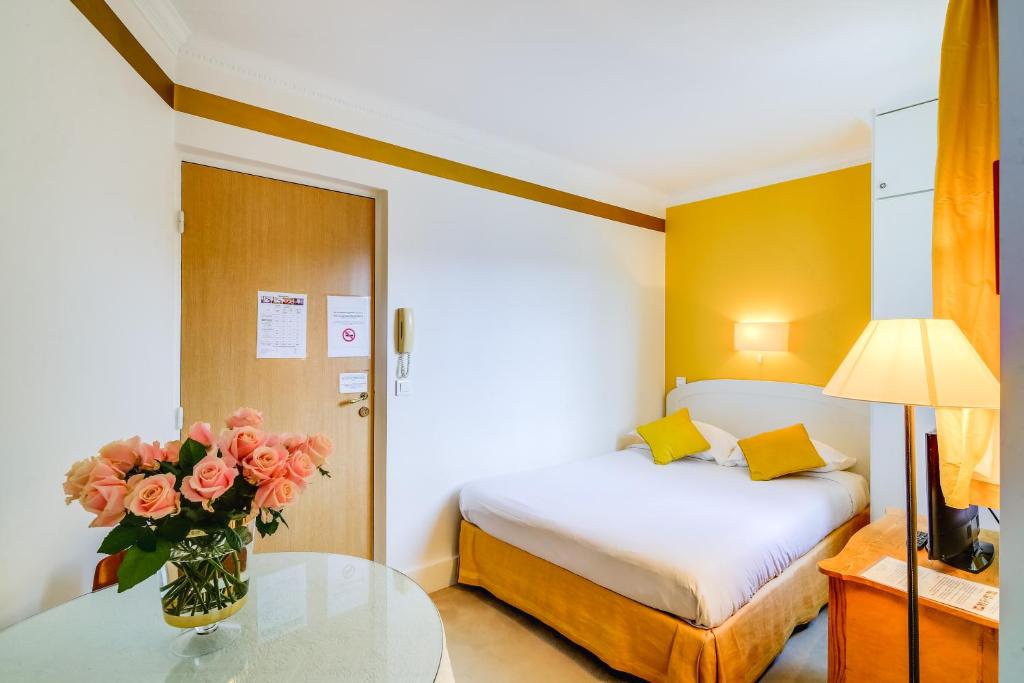 1 dormitorio con 1 cama y un jarrón de flores sobre una mesa en Villa Escudier Appart-hôtel en Boulogne-Billancourt