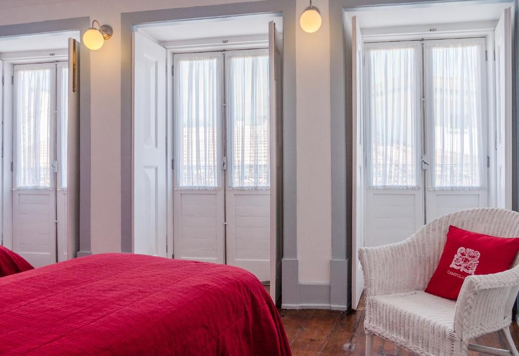 a bedroom with a bed and a chair and windows at Baga de Sal Wine Guesthouse in Aveiro