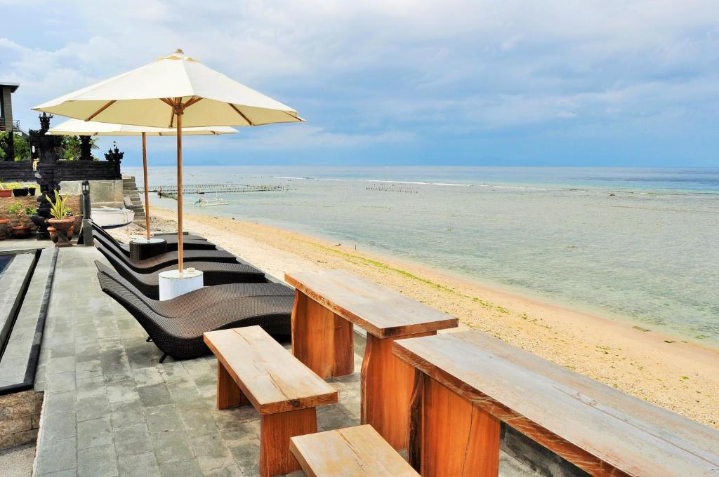 ペニダ島にあるPradana Beach Inn Luxuryの木製のベンチとパラソルが備わるビーチ